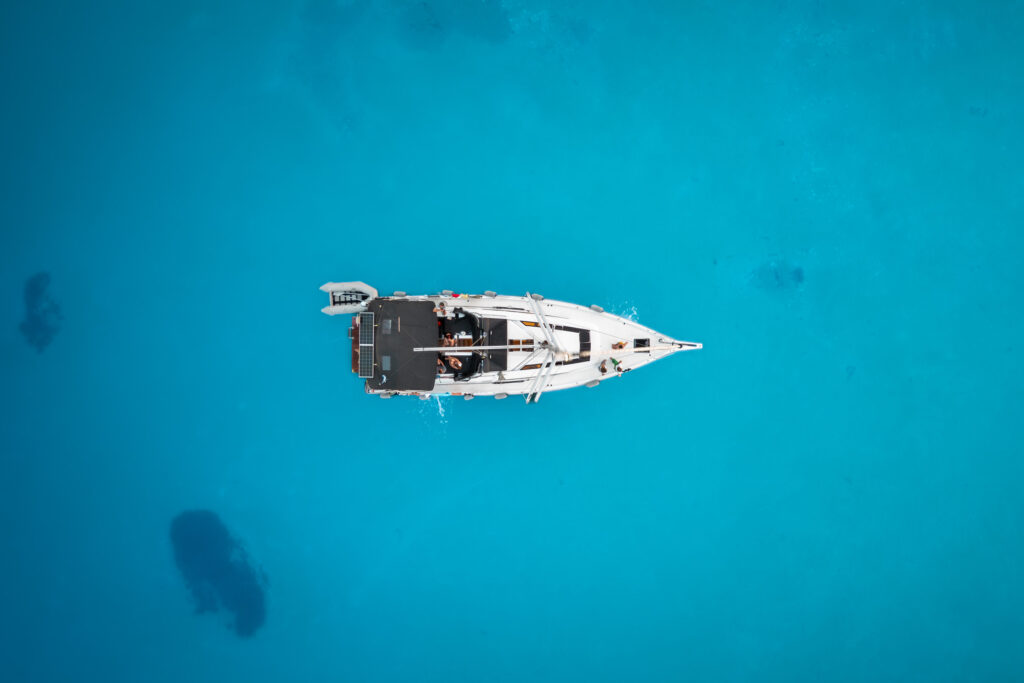 Luftaufnahme eines einzelnen weißen Segelboots, das in klarem, leuchtend blauem Wasser schwimmt. Das Boot befindet sich in der Bildmitte, umgeben von der unendlichen Weite des Meeres, und zeigt seine Ruhe und Abgeschiedenheit – eine heitere Segeltour auf ruhigem Wasser. Segeln und Yoga auf Mallorca: Die entspannendsten Routen und Buchten