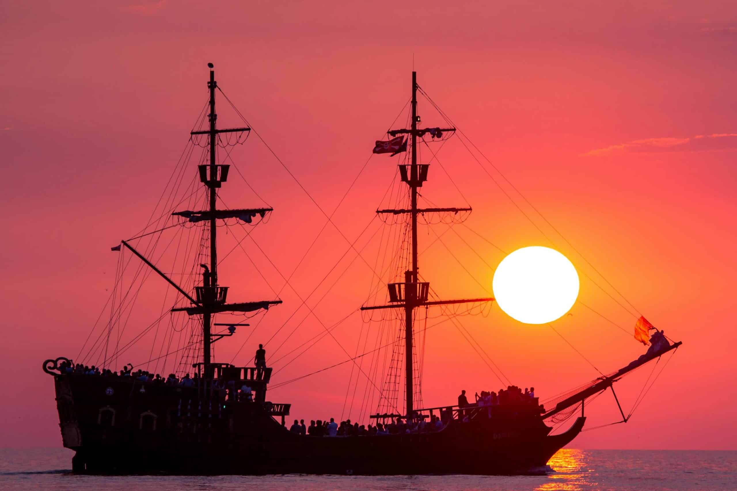 Silhouette of a Pirate Ship Sailing on Sea during Golden Hour. Wie im Film Fluch der Karibik, welcher perfekt für einen Winterfilmeabend ist, wenn man sich nach dem Segeln und Meer sehnt. 