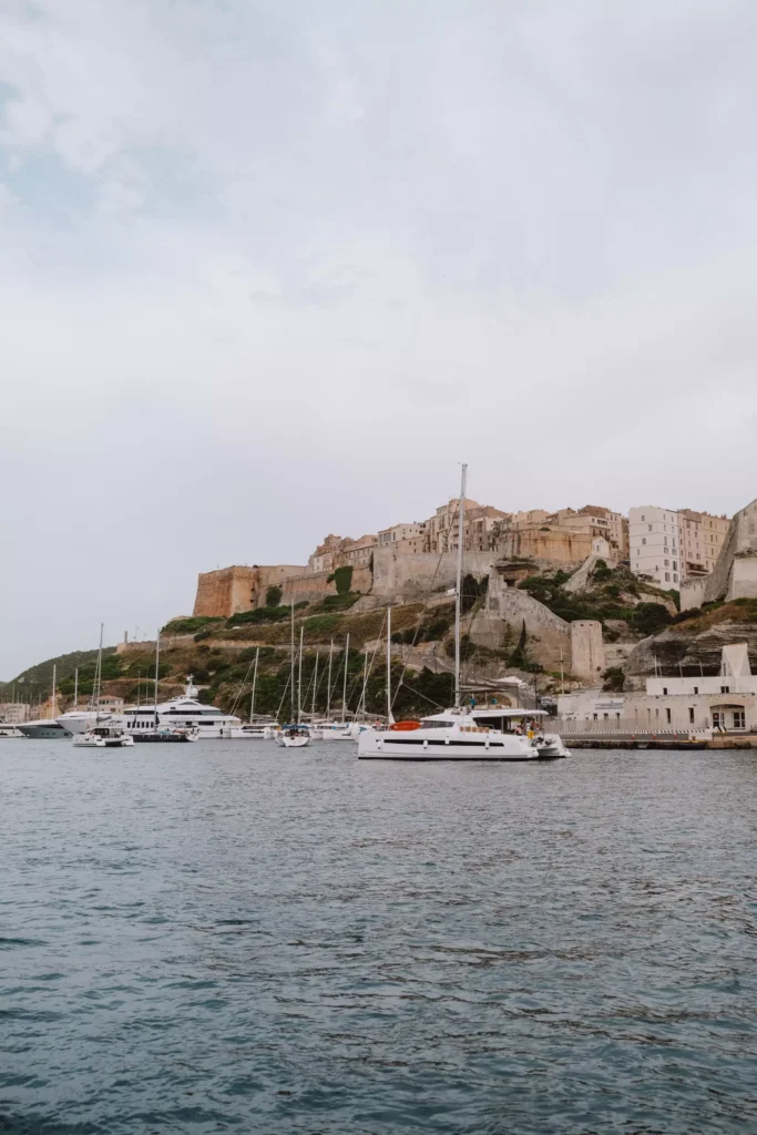 Yachten und Segelboote vertäut im Hafen mit einer hoch aufragenden, alten Zitadelle auf einem Hügel im Hintergrund unter einem bewölkten Himmel während ihres Segeltörns.
