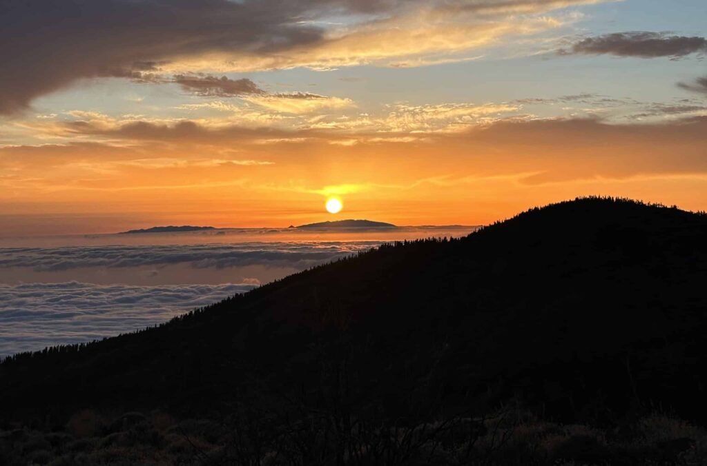 Der Teide, Spaniens höchster Berg, ist ein Muss für jeden Fotografen auf Teneriffa. Der Nationalpark Teide bietet beeindruckende Landschaften, von vulkanischen Felsen bis hin zu kargen Hochlandflächen. Die surrealen Farben und Formen der Umgebung sind atemberaubend und ideal für Landschaftsfotografie. Zu sehen ist ein harmonische Sonnenuntergang über den Wolken. Die Wolken haben sich schon gelb verfärbt. Die athmosphäre wirkt sehr romantisch.