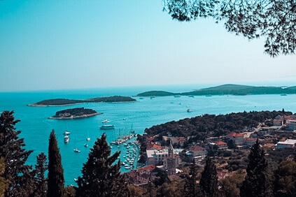 Eine malerische Aussicht auf eine Küstenstadt mit Blick auf ein klares blaues Meer mit mehreren Inseln und Segelbooten, an den Rändern von Laub eingerahmt.